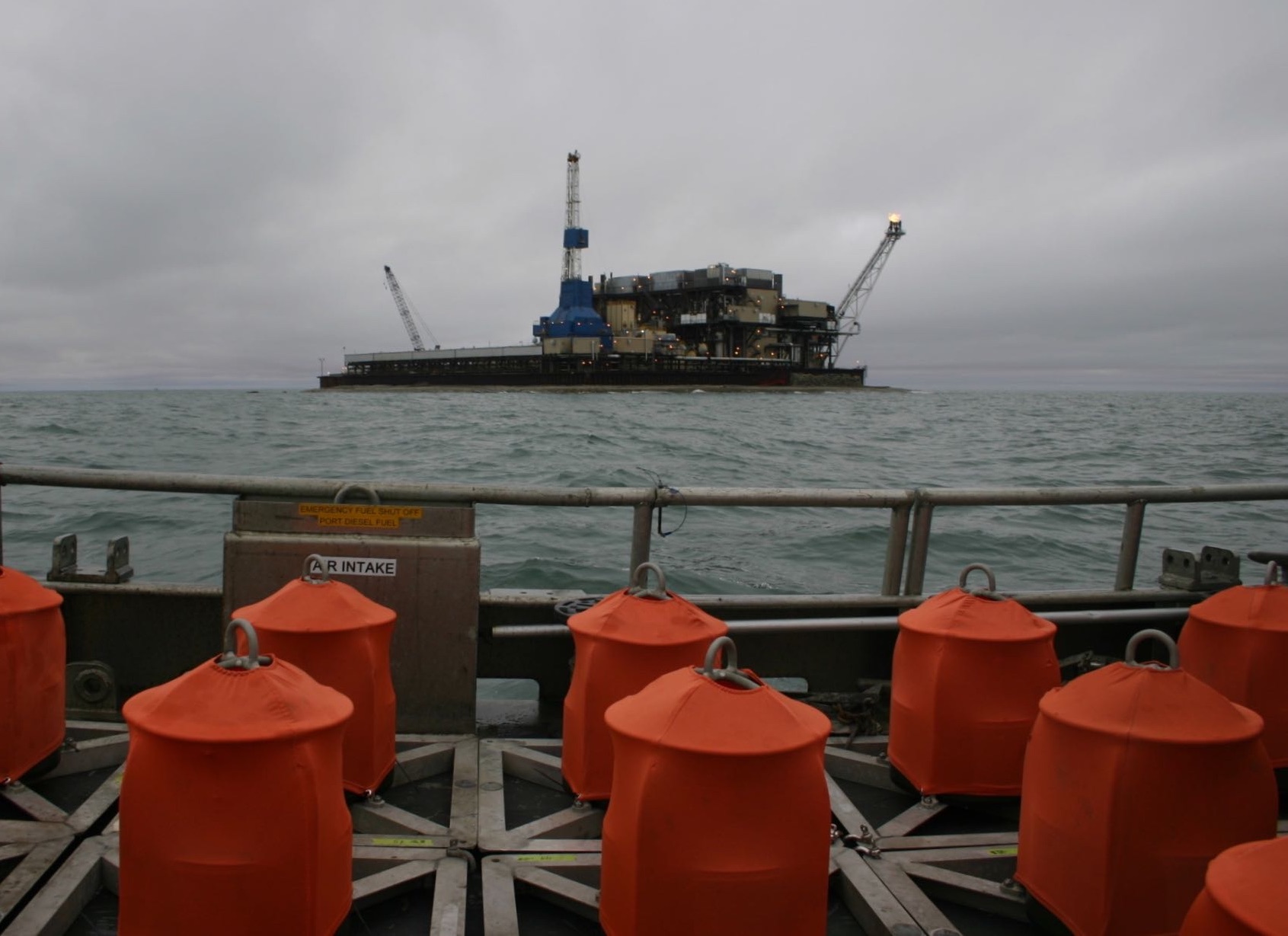 Directional Autonomous Seafloor Acoustic Recorders (DASARs), clad in their orange shrouds, on the deck of a vessel while waiting to be deployed onto the seafloor near an oil production island in the Beaufort Sea. -2018 DASARs in front of oil production island